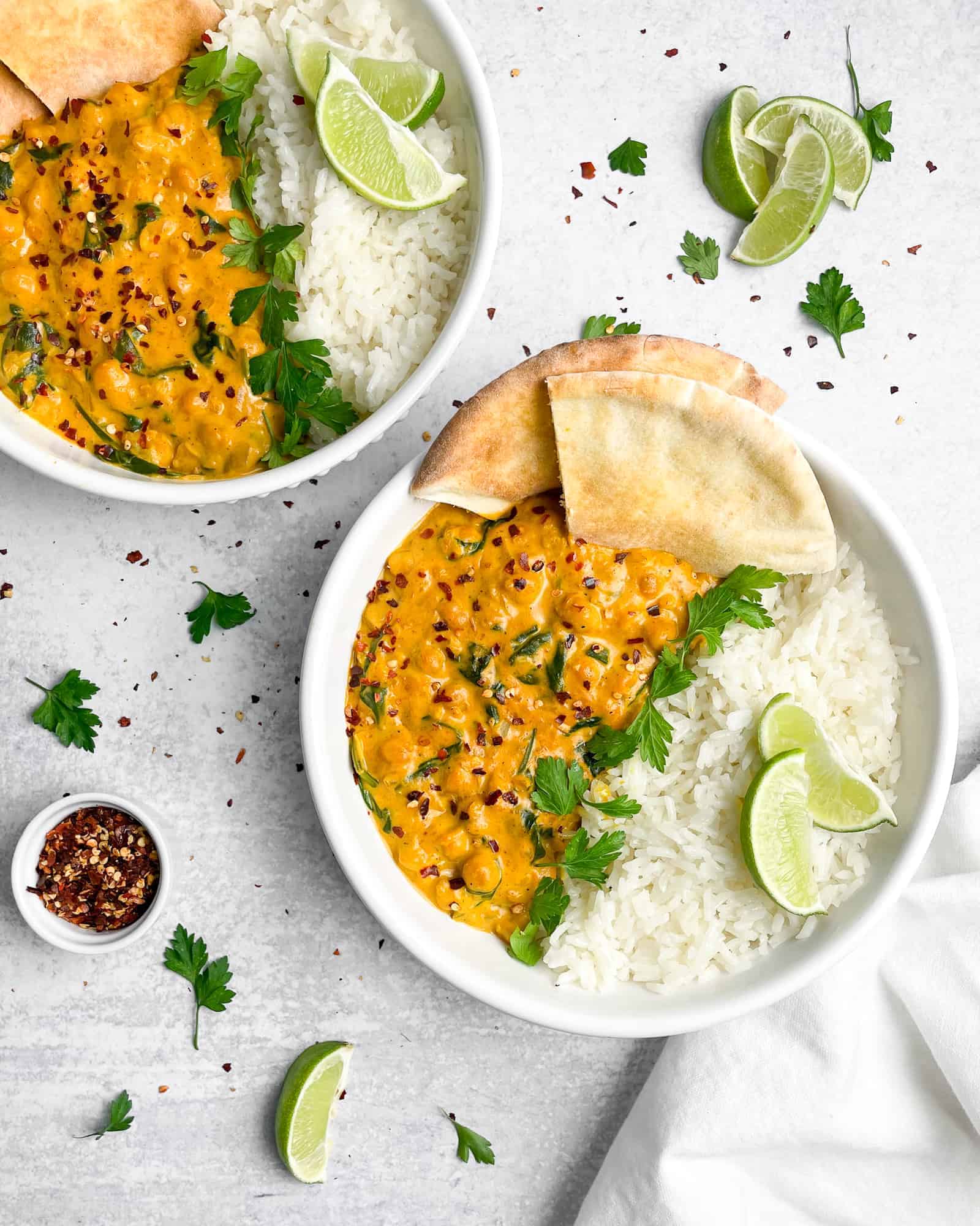 chickpea spinach curry over rice in a white bowl topped with red pepper flakes and cilantro.