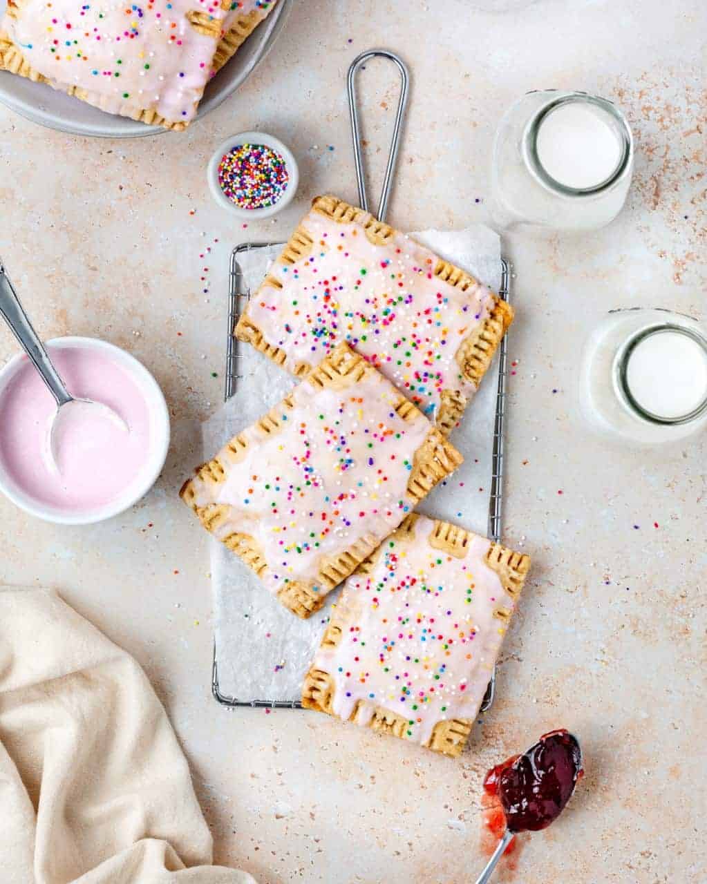 Homemade Vegan Strawberry Poptarts topped with pink vanilla icing and sprinkles on a cooling rack.