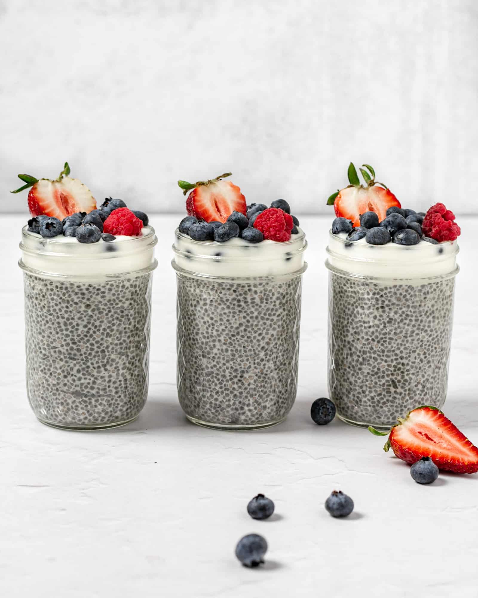 3 chia seed puddings in mason jars topped with fresh fruit and yogurt lined up next to each other.