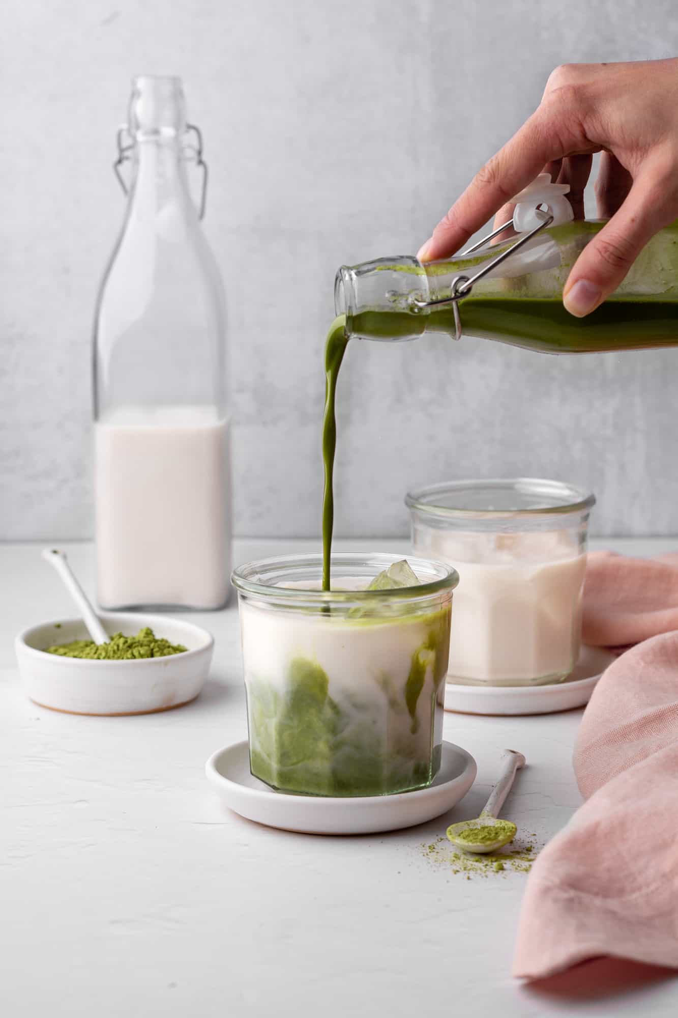 pouring matcha paste into a glass filled with milk and ice to make iced matcha green tea latte