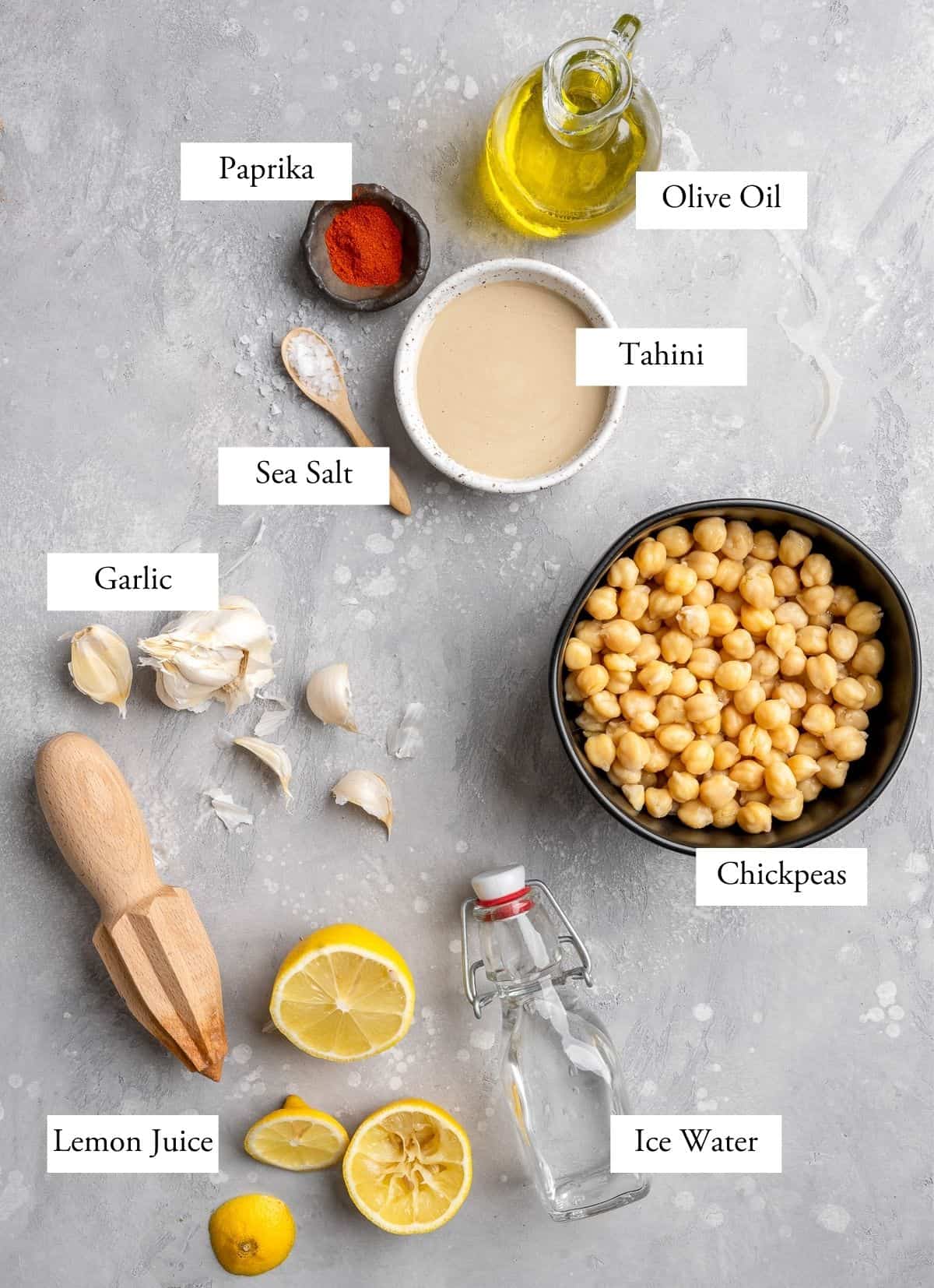roasted garlic hummus ingredients on a table labeled - ice water, lemon juice, chickpeas, paprika, garlic, sea salt, tahini, olive oil