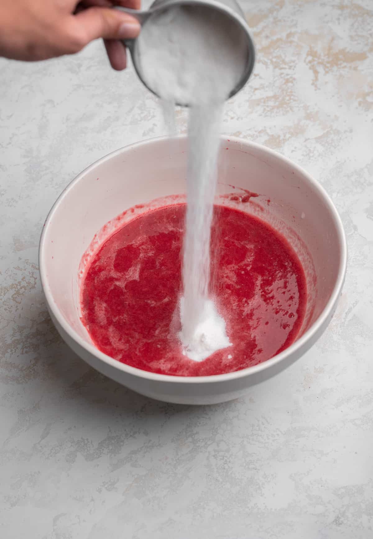 Sugar being poured into raspberry puree
