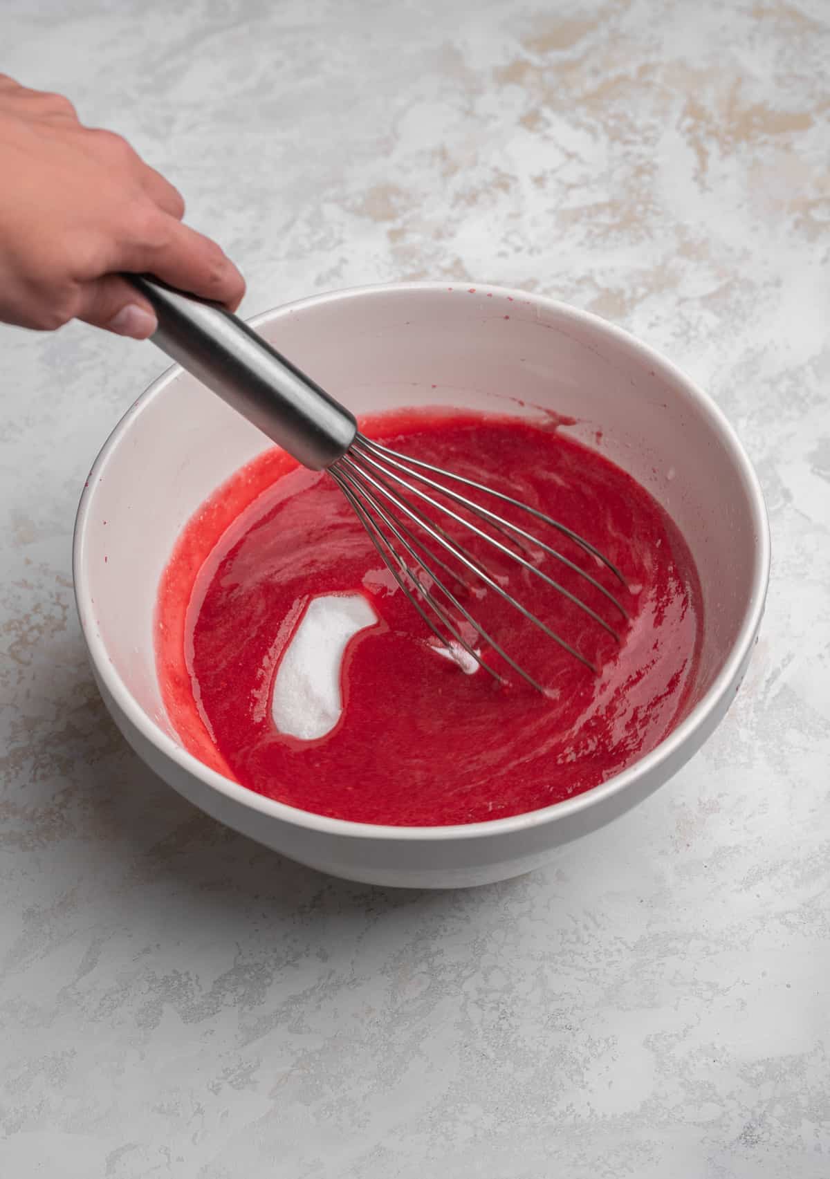 Raspberry puree and sugar being whisked in a bowl