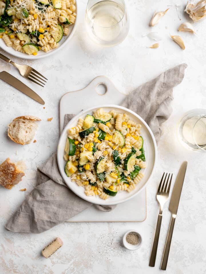 vegan creamy summer pasta with zucchini, corn and spinach on a white plate topped with parmesan cheese