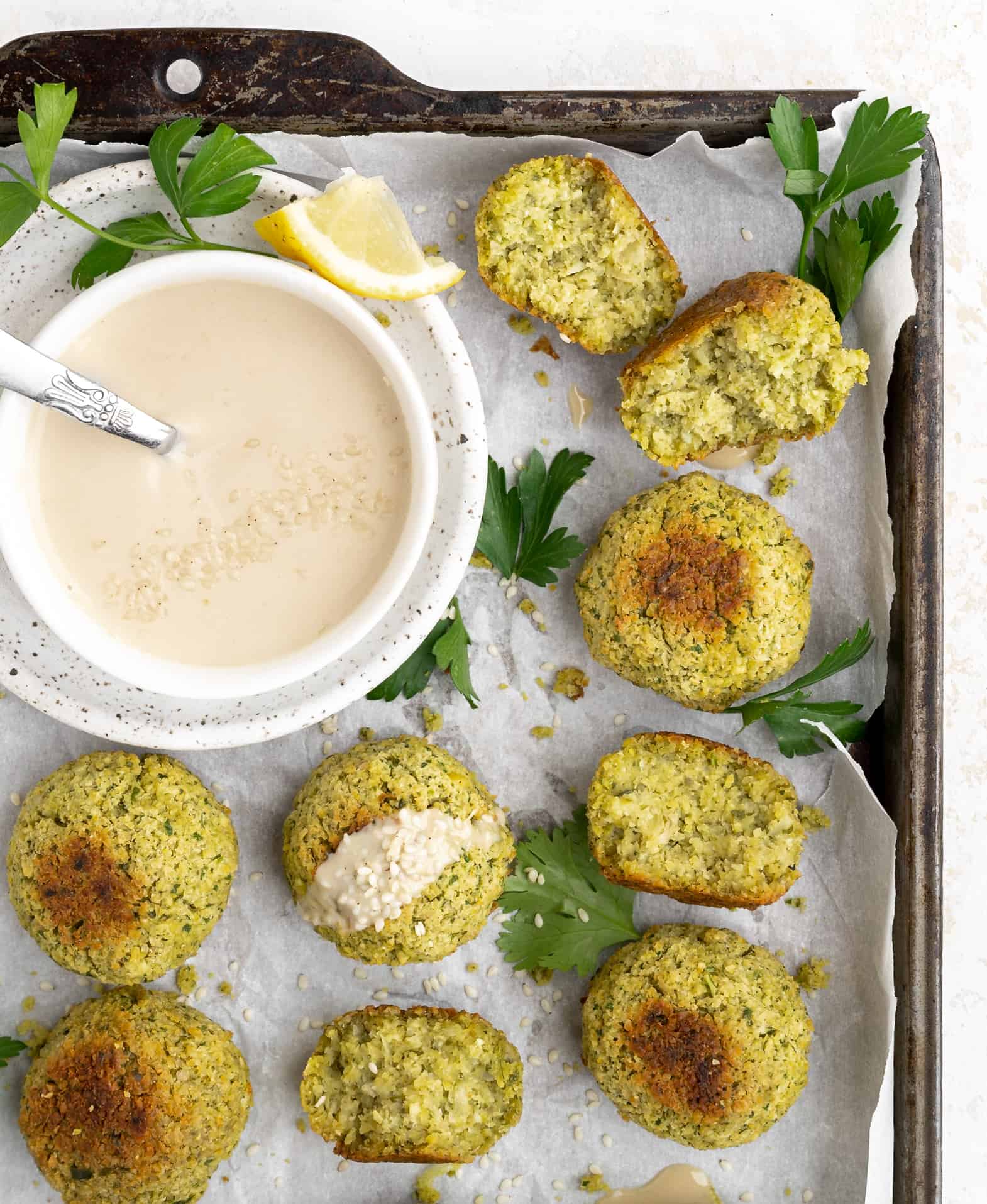 Baked falafel on a baking sheet with tahini sauce