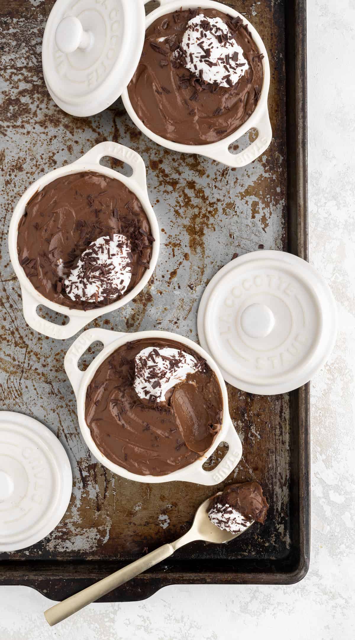chocolate avocado mousse with a scoop of coconut cream on top divided into 3 white ramekins