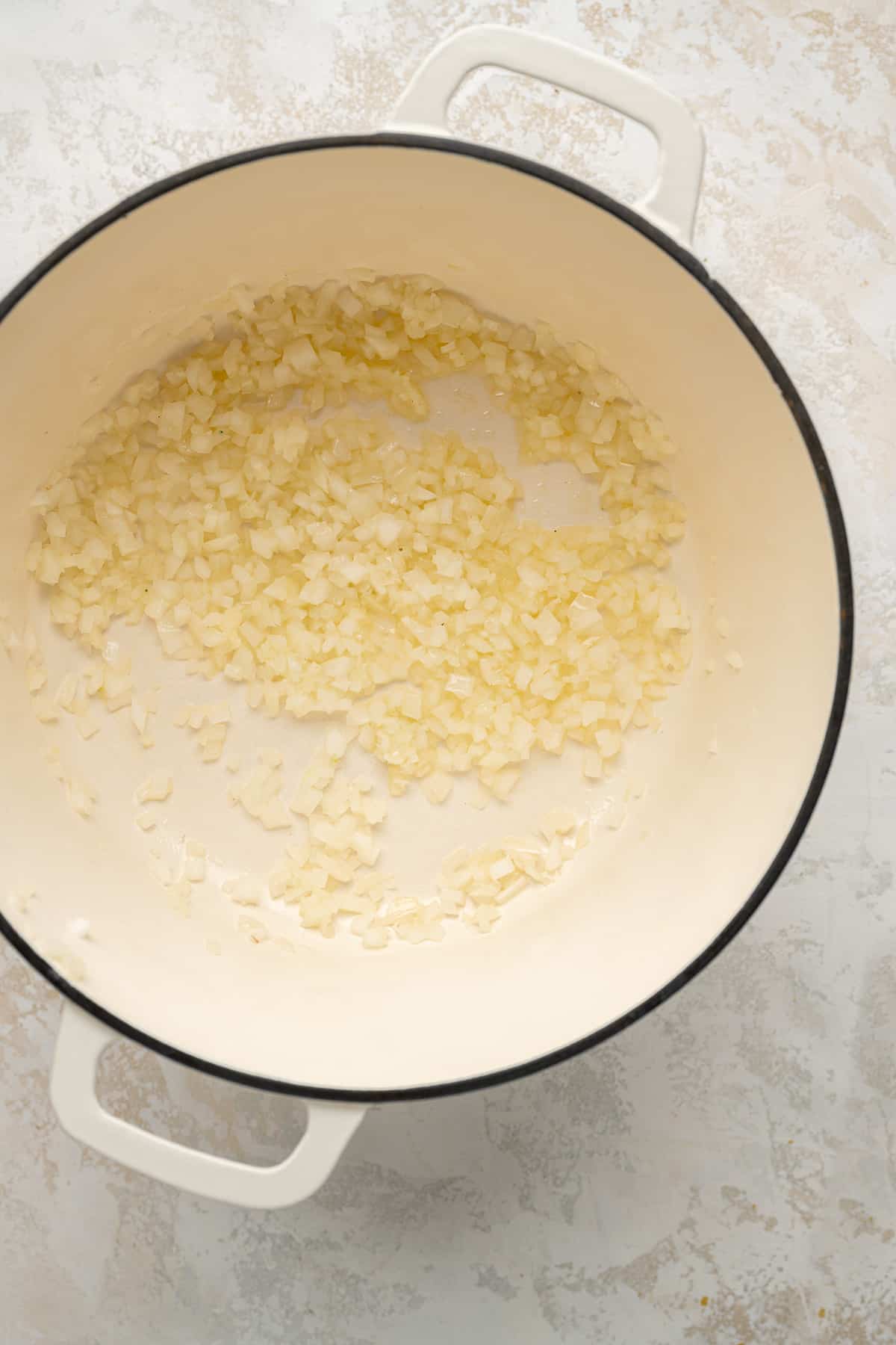 Onions and garlic being sauteed in a white dutch oven pot.