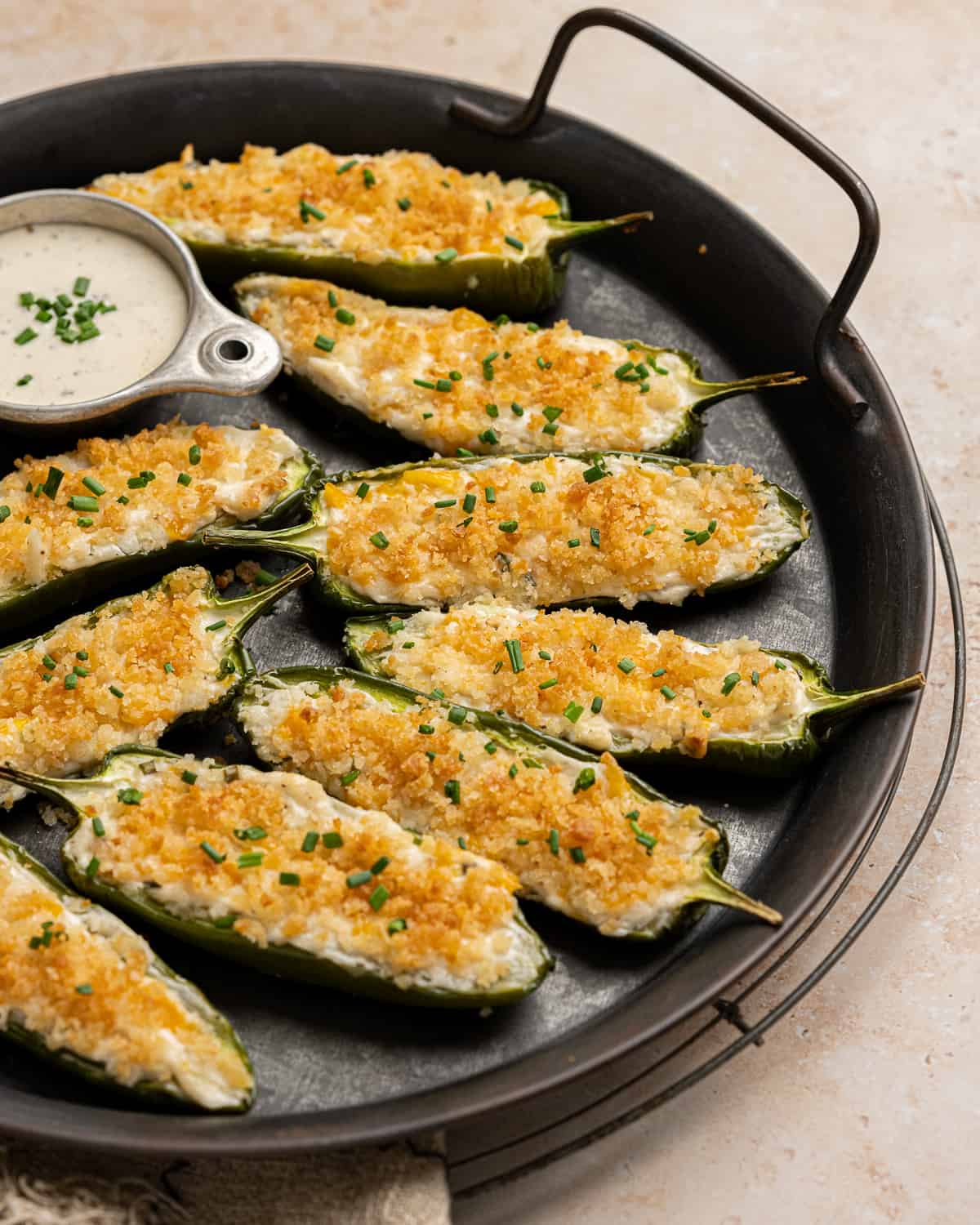 close up of jalapeno poppers topped with bread crumbs and chives on a serving tray.
