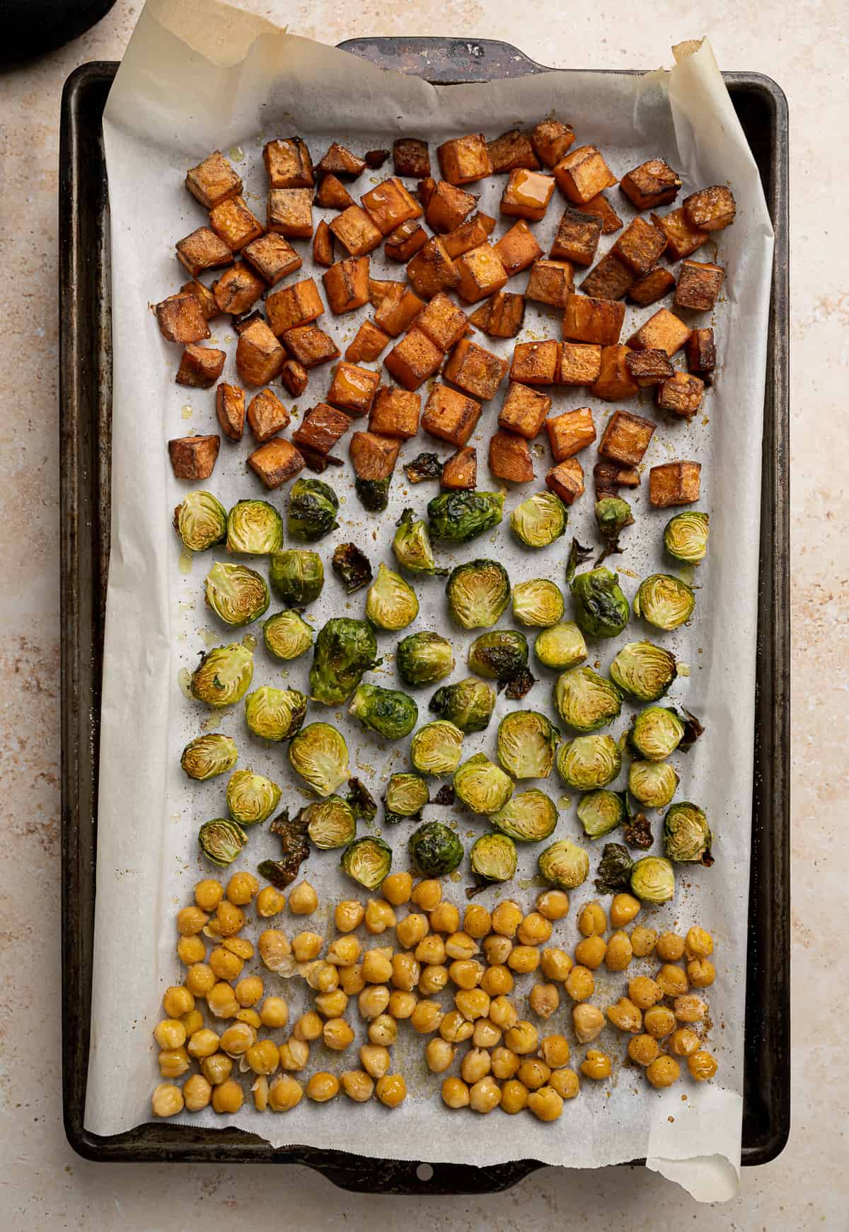 roasted sweet potatoes, brussel sprouts, and chickpeas on a baking sheet.