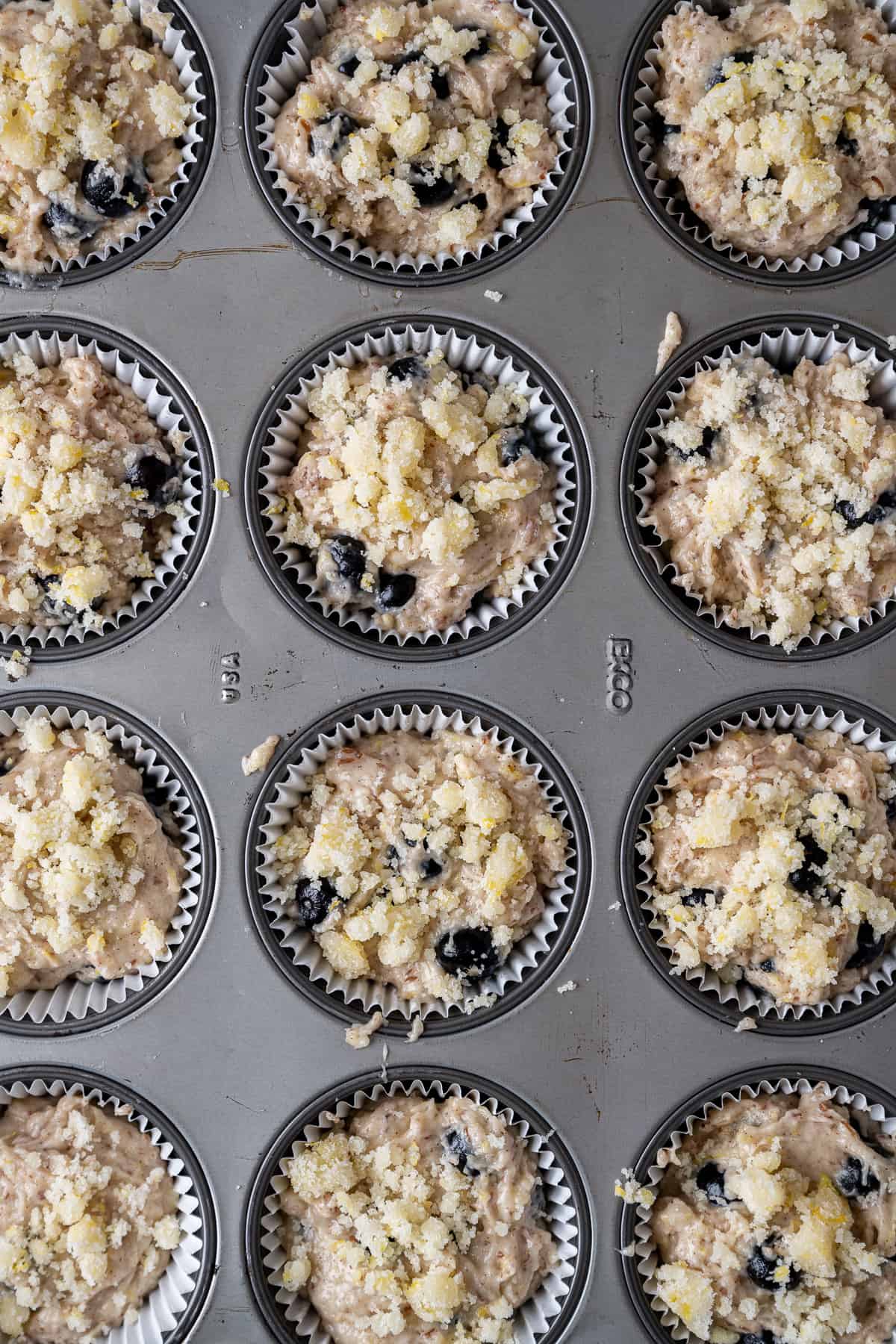Lemon blueberry muffins topped with streusel in muffin tins.