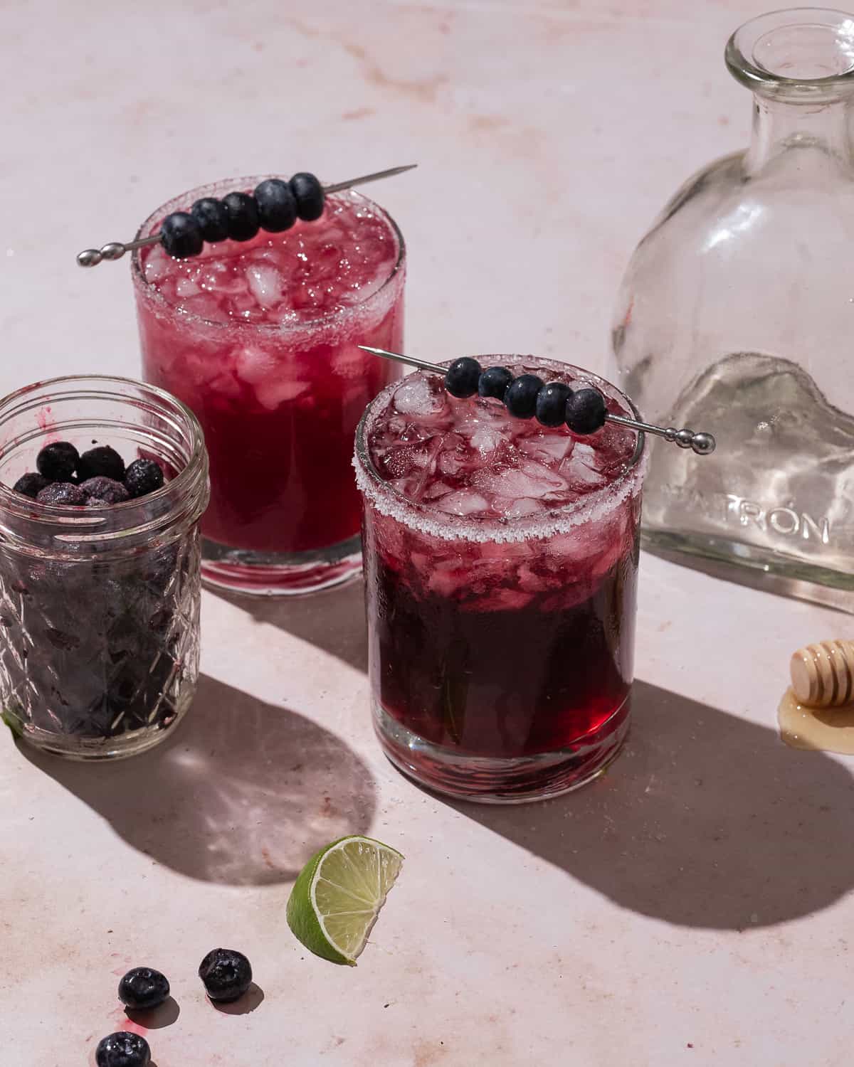 blueberry pomegranate margaritas with a cocktail pick filled with blueberries.