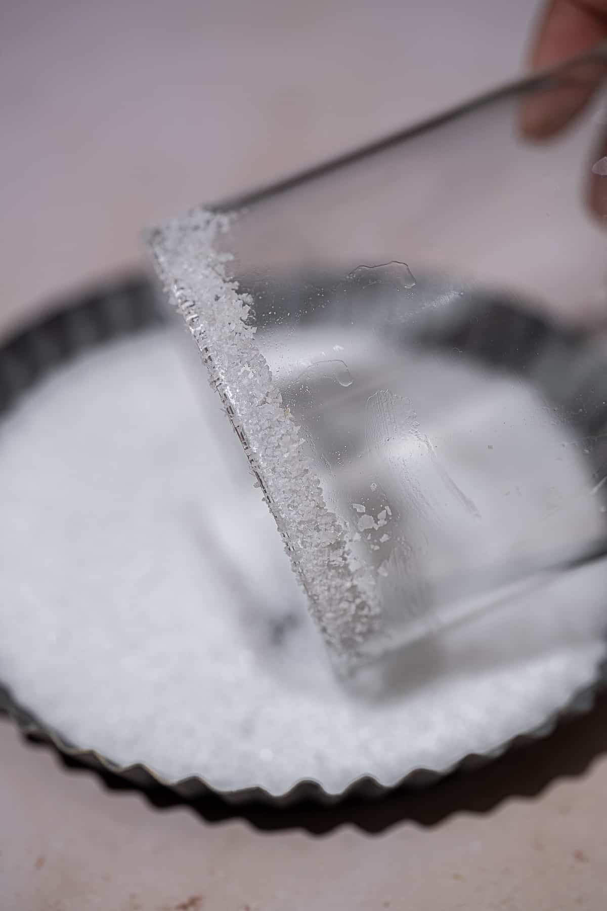 Rim of cocktail glass being rolled in kosher salt.