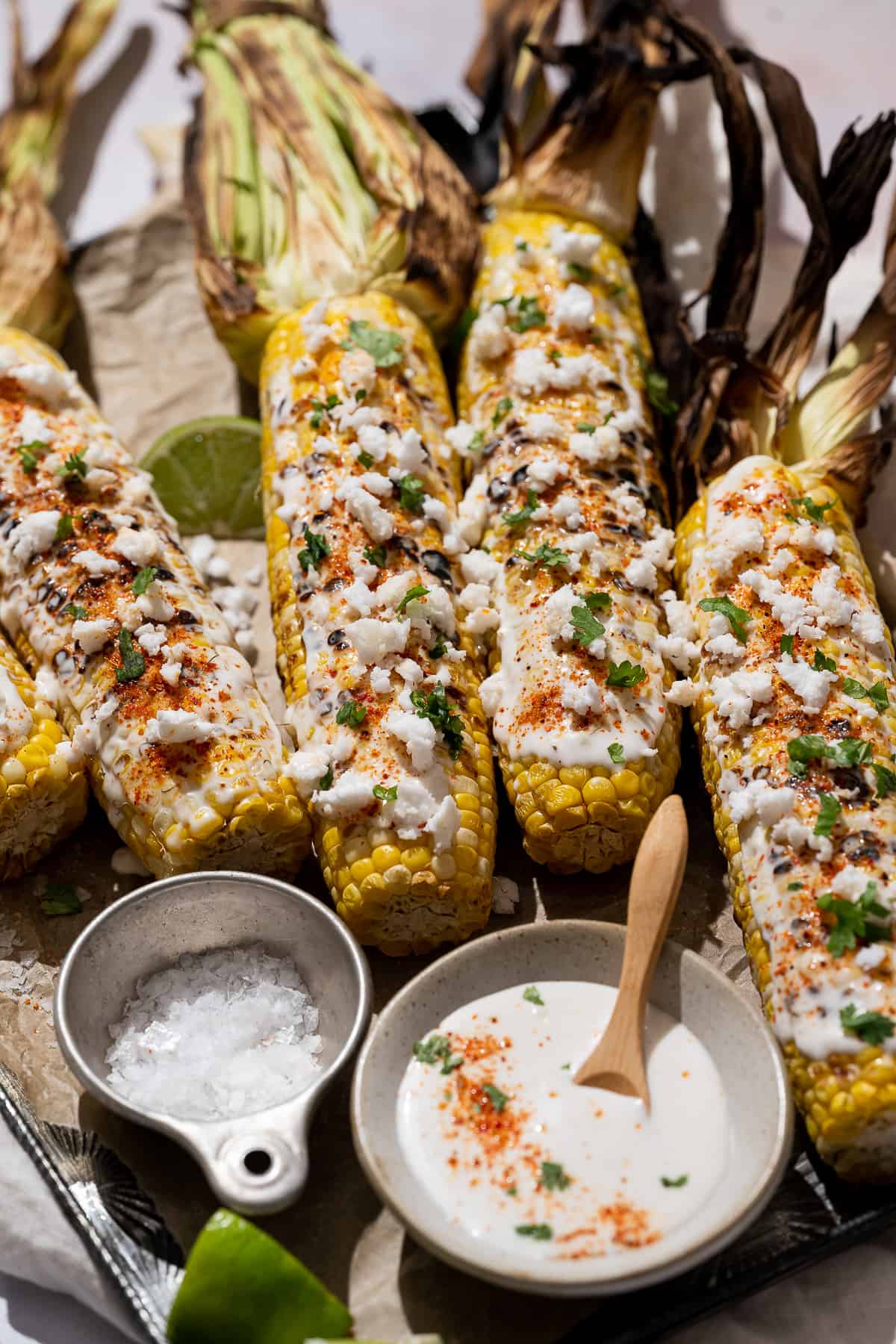 grilled corn on a sheet pan topped with mexican toppings.