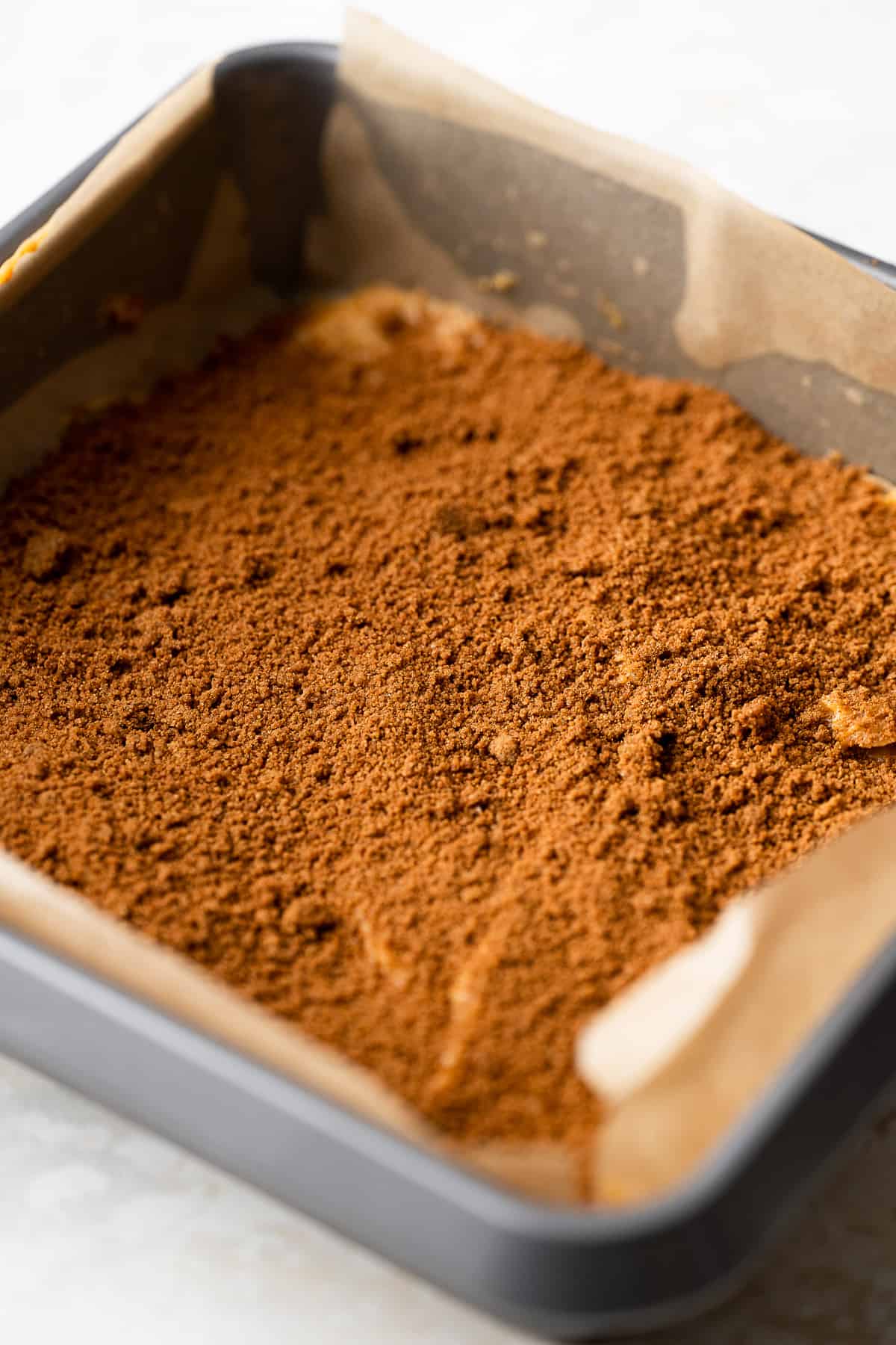 cinnamon sugar being spread across the first layer of pumpkin cake batter.