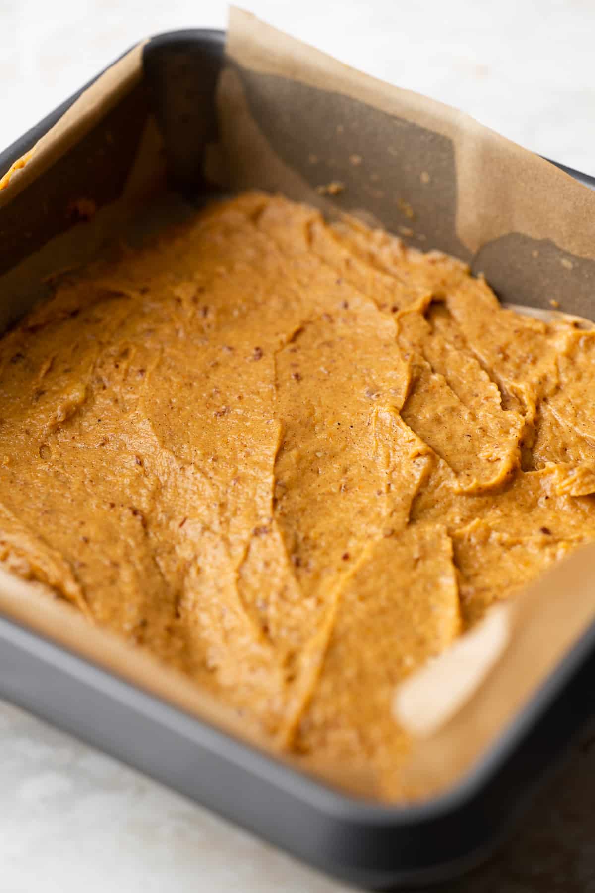 first layer of pumpkin cake batter spread in a baking dish lined with parchment paper.