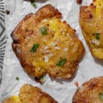close up of crispy smashed potatoes topped with sea salt and chopped parsley on parchment paper.