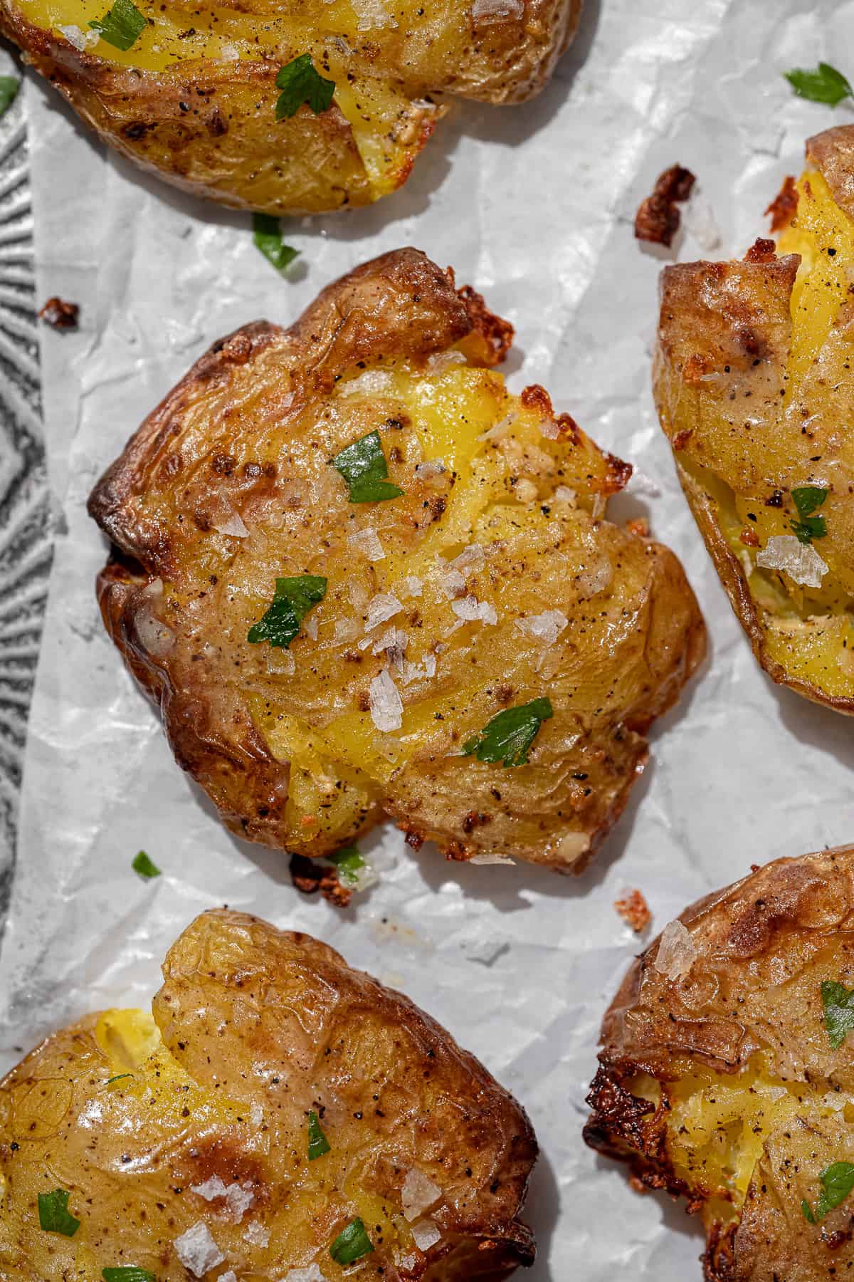 close up of crispy smashed potatoes topped with sea salt and chopped parsley on parchment paper.