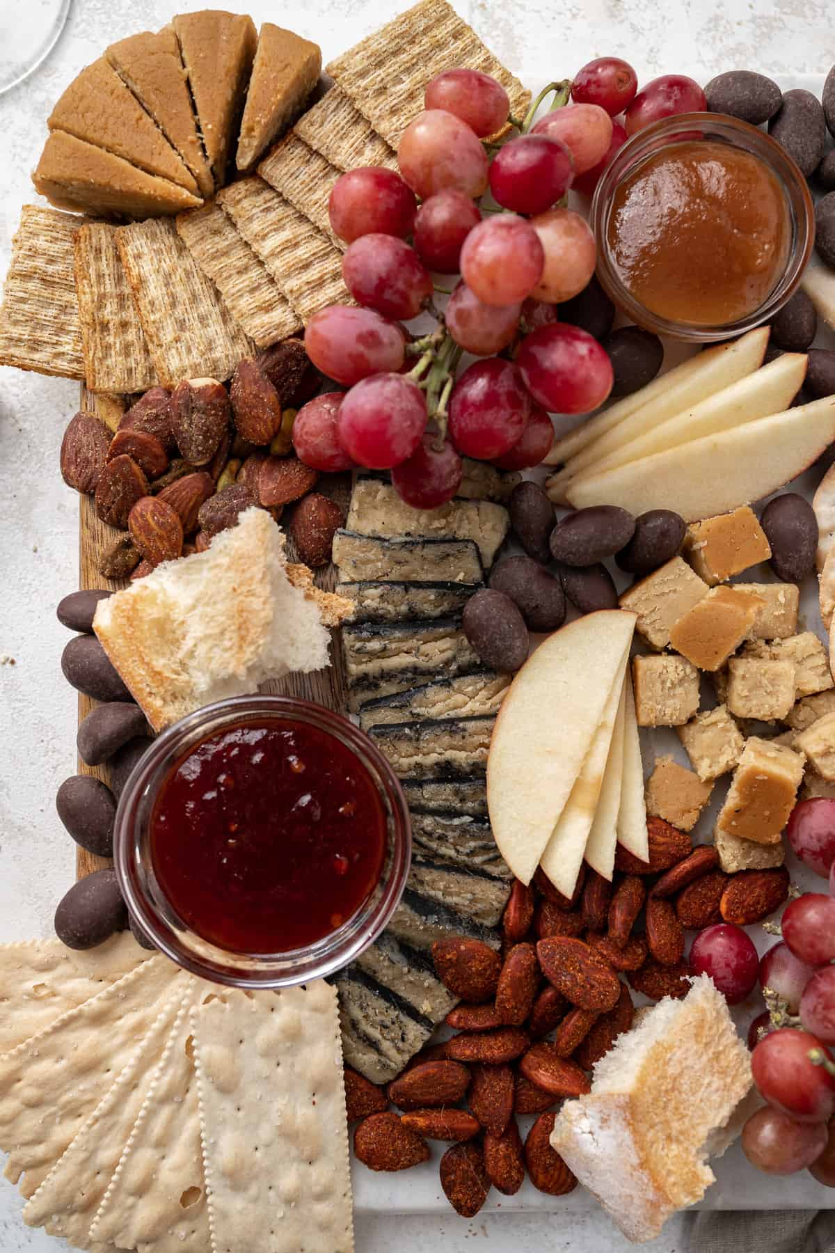 close up of vegan cheeses, crackers, fruit and jams on a charcuterie board.