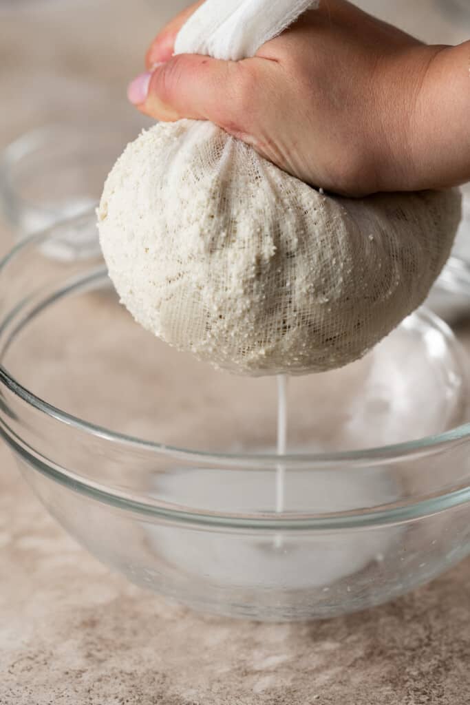Cheesecloth filled with tofu being squeezed to drain excess liquid.